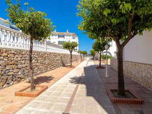 A paved pathway flanked by stone walls and trees, leading to a white building with a tiled roof. - Las Fuentes Torrecilla by Casasol by Interhome (Nerja)