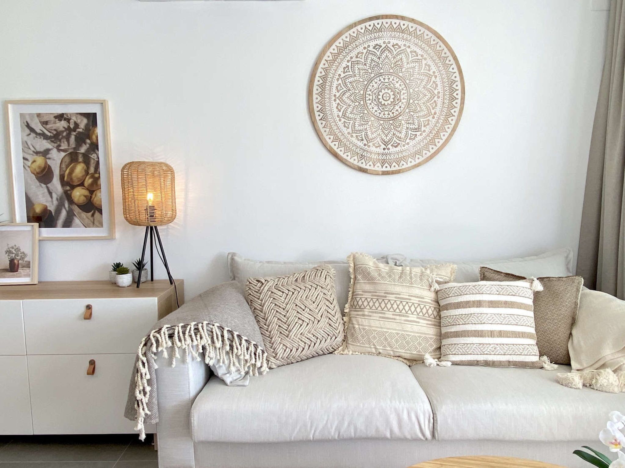A modern living room with a white sofa, a round wall hanging, a floor lamp, and a framed picture on a side table.
