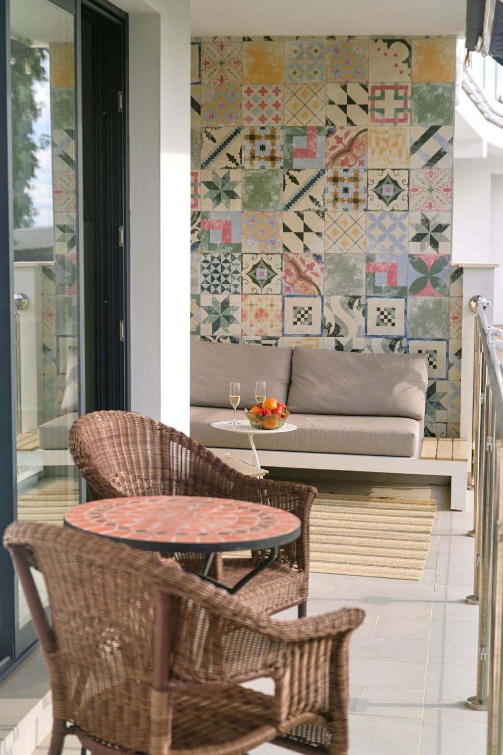 A balcony with wicker furniture, a patterned wall, and a sofa with a fruit bowl.