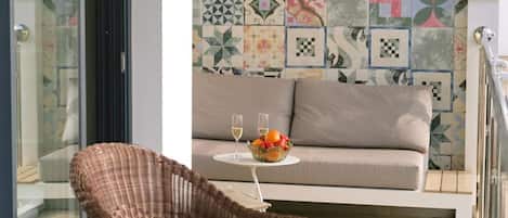 A balcony with wicker furniture, a patterned wall, and a sofa with a fruit bowl.