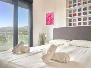 Ein Hotelzimmer mit großem Fenster, einem Bett mit weißer Bettwäsche, einem grauen Kopfteil und einer Wand mit einer Ansammlung gemusterter Fliesen.