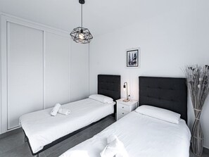 Ein modernes Schlafzimmer mit zwei Betten, einem Nachttisch, einer Wandleuchte und einem gerahmten Bild.