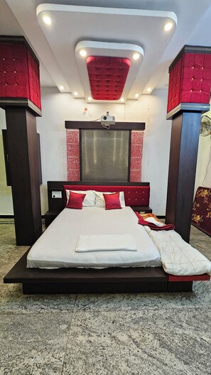 A modern bedroom with a large bed, a ceiling projector, and a red accent wall. - Hotel SRB Suites (Tirupati)