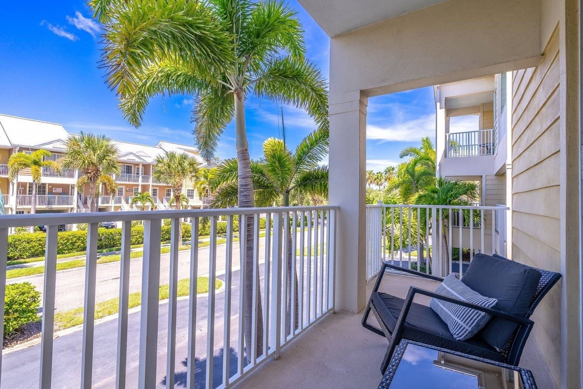 A balcony with a view of a residential area, including palm trees and a multi-story building.