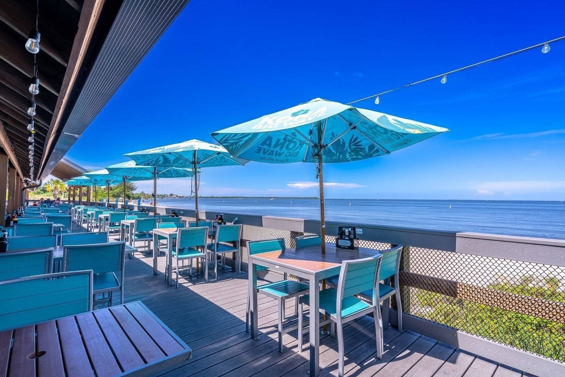 An outdoor seating area with tables and chairs, umbrellas, and a view of the ocean.