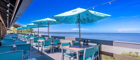 An outdoor seating area with tables and chairs, umbrellas, and a view of the ocean.