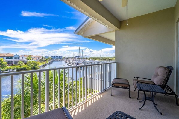 A balcony with a view of a marina and a river, furnished with a chair and a table.