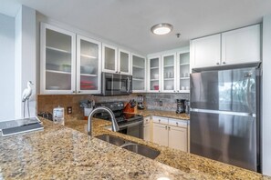 A modern kitchen with white cabinets, stainless steel appliances, granite countertops, and a built-in oven.