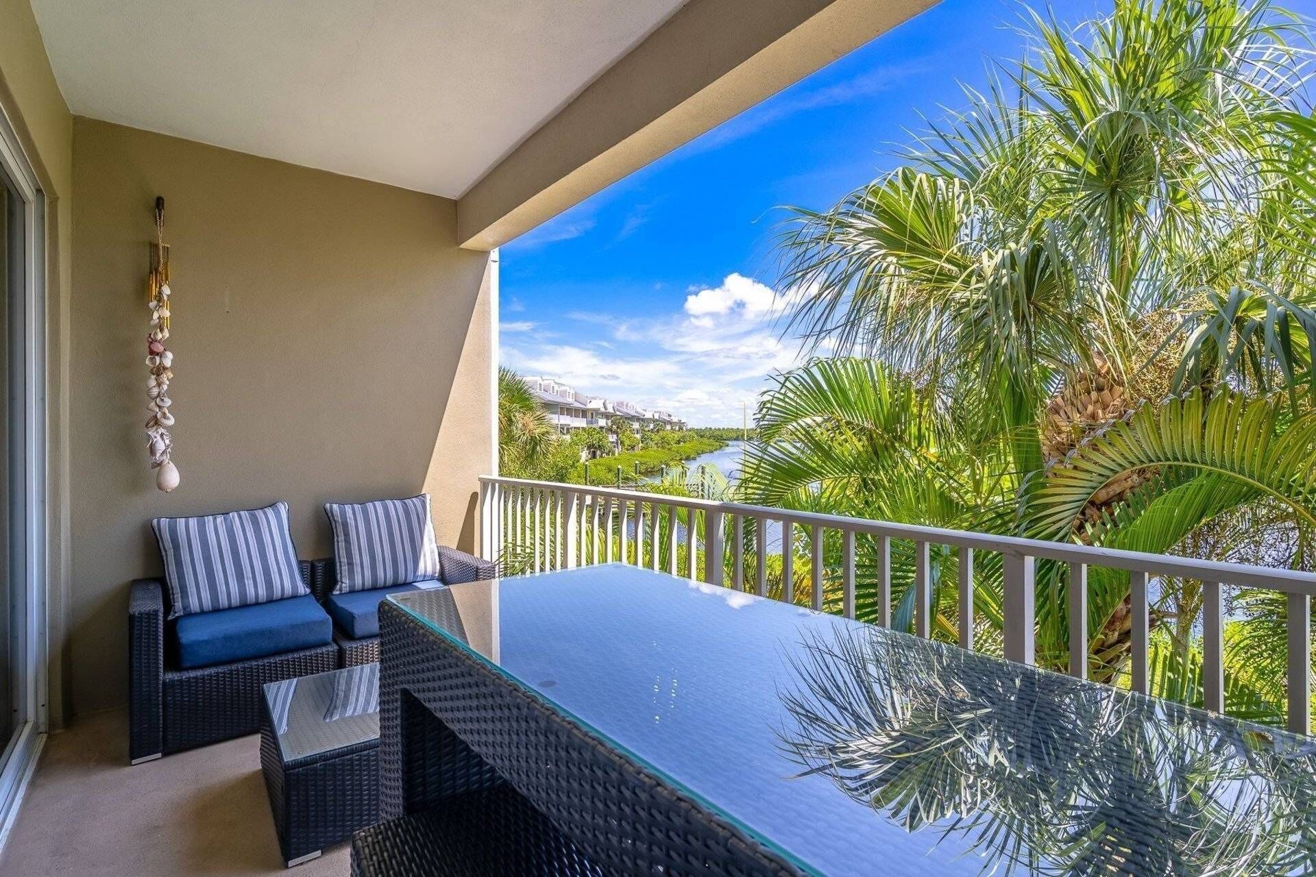 A balcony with a glass-top table, two cushioned chairs, and a decorative hanging.