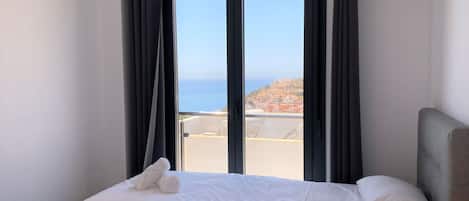 Una habitación de hotel con cama, ventana con cortinas y vista al mar.
