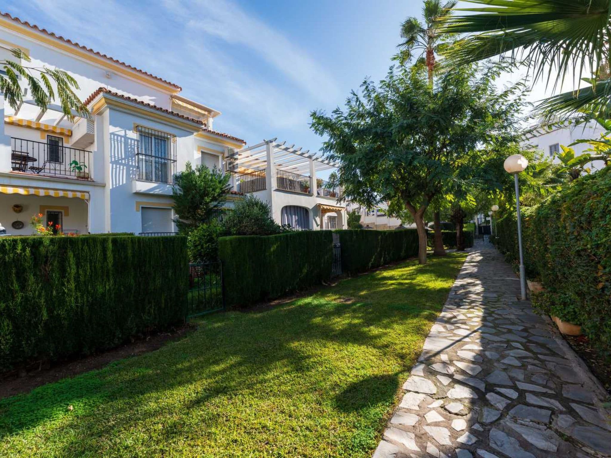 A residential area with a stone pathway, well-maintained lawn, and houses with balconies.