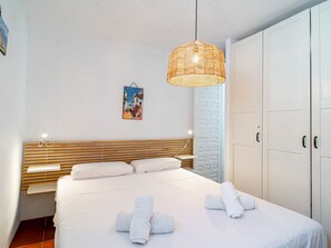 Ein Hotelzimmer mit Bett, Kopfteil, Nachttisch, Pendelleuchte, Kleiderschrank und einem an der Wand hängenden Gemälde.