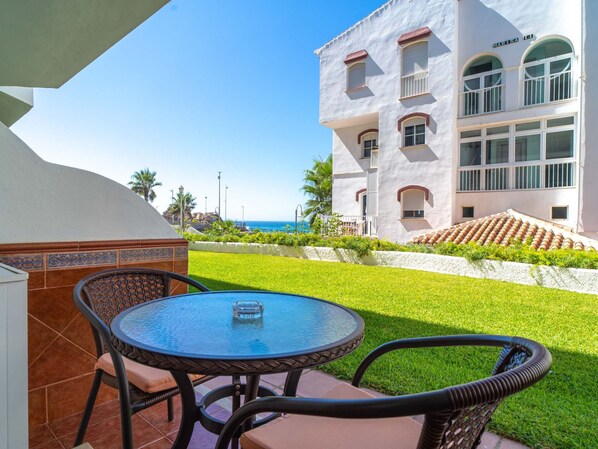 Eine Terrasse mit rundem Tisch und Stühlen, ein weißes Gebäude mit Balkonen und freier Meerblick.