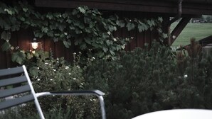 Una panchina sotto una struttura in legno con un lampadario, circondata dal verde.