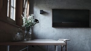 Una stanza con un tavolo, un vaso con fiori, una lampada a parete e una televisione.