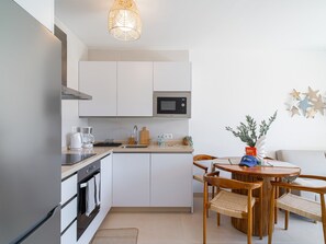 Eine moderne Küche mit weißen Schränken, einer Mikrowelle und einer Kaffeemaschine. Es gibt einen Essbereich mit Holzkohle und einem Tisch.