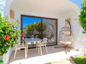 Eine Terrasse im Freien mit Tisch und Stühlen, einem Hängesessel und einer Glastür, die in einen Garten führt.