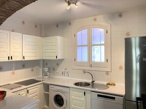 A compact kitchen with white cabinetry, a built-in washing machine, a stainless steel refrigerator, and a window with frosted glass. - Apartment  by Interhome (Nerja)