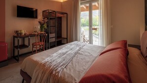 A bedroom with a bed, a desk, a chair, a TV, and a balcony with a view.