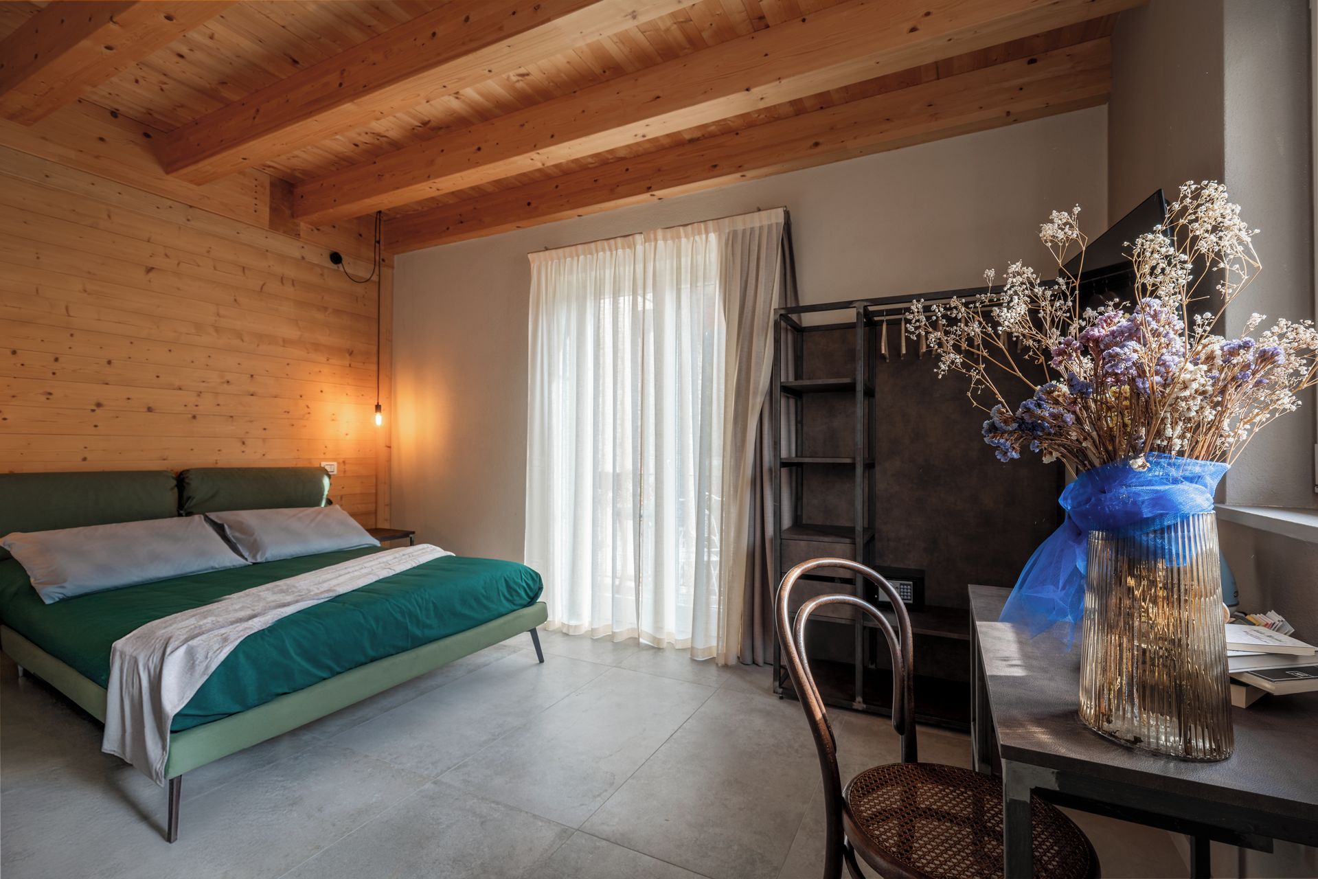 Ein Zimmer mit einem Bett, einem Sessel, einem Schreibtisch und einem Fenster mit Vorhängen.