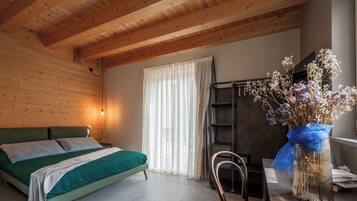 Ein Zimmer mit einem Bett, einem Sessel, einem Schreibtisch und einem Fenster mit Vorhängen.