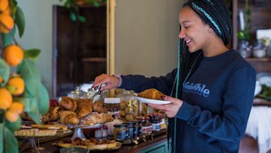 A person serving food from a buffet with various pastries and condiments.