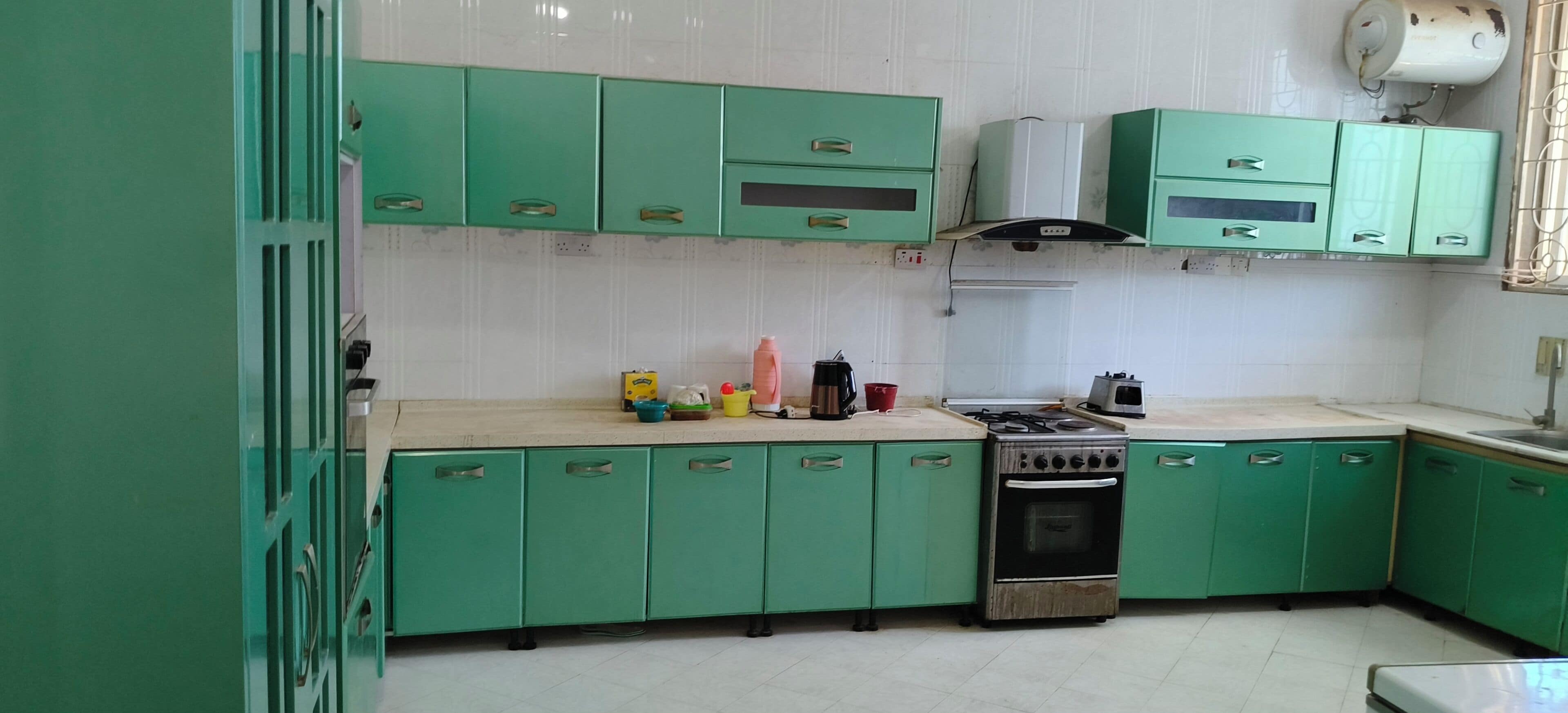 Une cuisine avec des meubles de rangement verts, une cuisinière et divers appareils de cuisine.