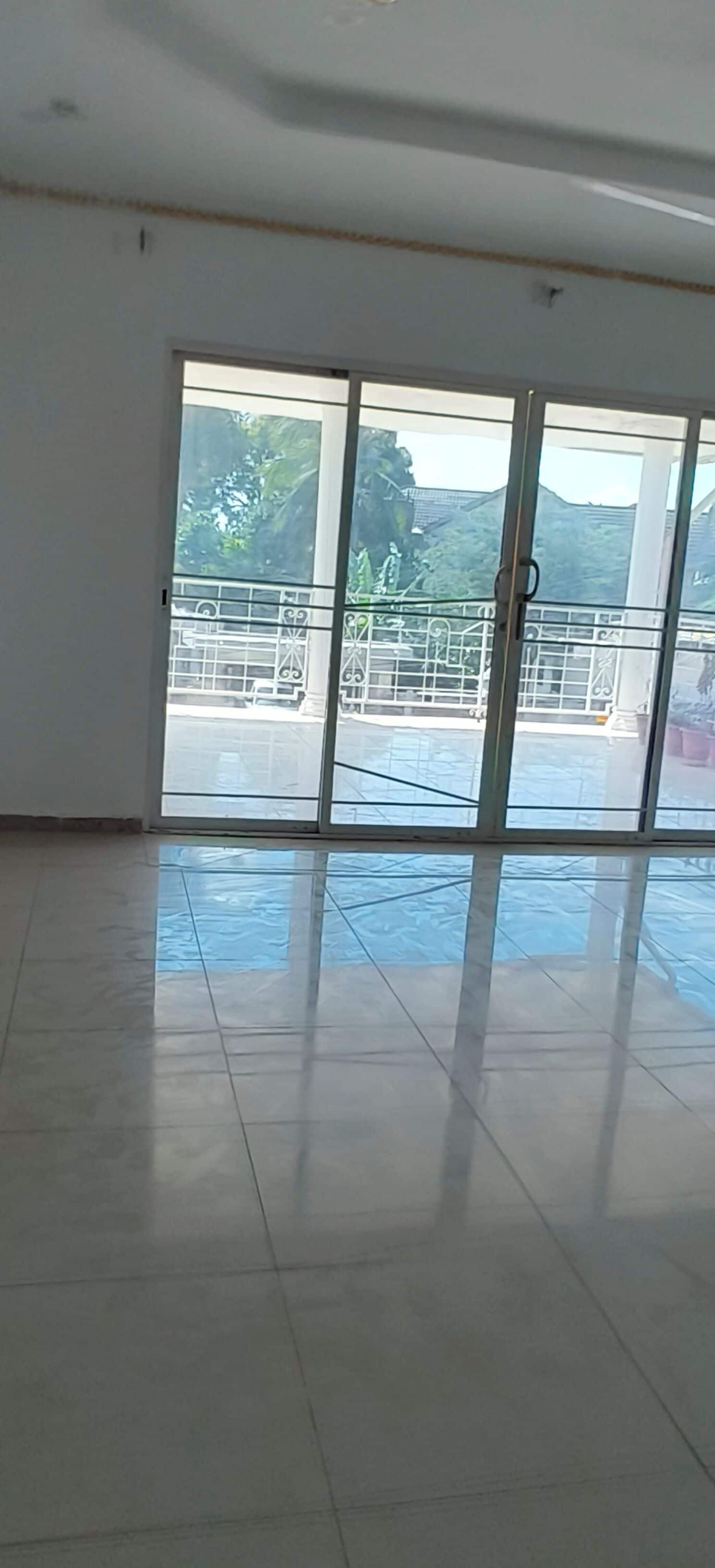 Amplia habitación con un gran ventanal corredero que da a un espacio exterior con barandilla metálica y follaje.