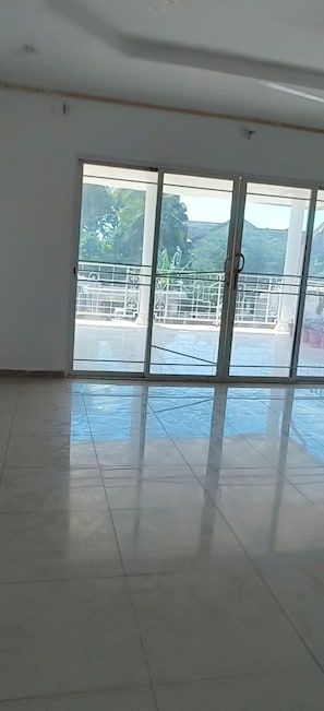 A spacious room with a large sliding glass door leading to an outdoor area with a metal railing and greenery.