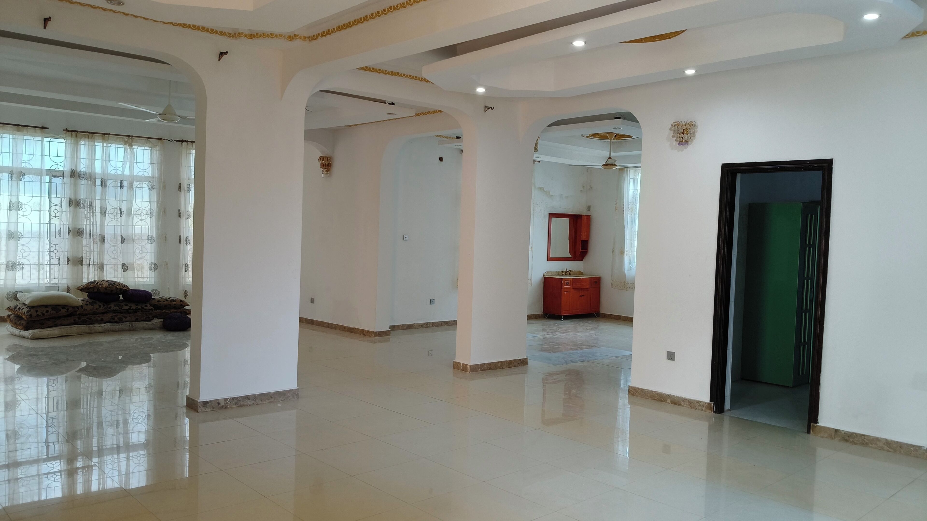 Un interior espacioso con techos altos, una columna central y una puerta que da a otra habitación.