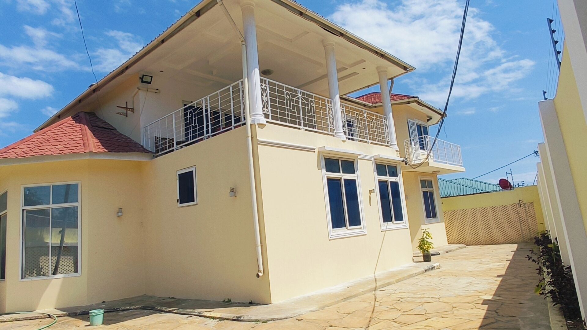 Um edifício de dois andares com varanda, telhado ladrilhado e área de entrada pavimentada.