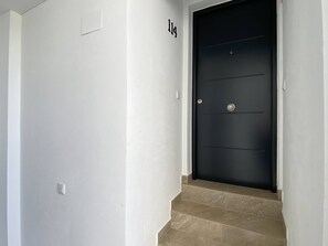 Ein Gang mit einer schwarzen Tür, einer weißen Wand und einem kleinen Satz beiger Stufen, die zur Tür hinaufführen.