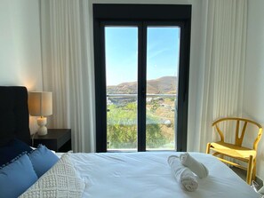 Ein Hotelzimmer mit einem Bett, einem Nachttisch, einer Lampe, einem Sessel und einem großen Fenster mit Landschaftsblick.