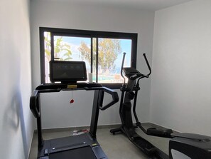 Ein Laufband und ein Crosstrainer in einem Raum mit Blick auf einen Pool und Palmen.