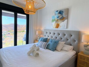 Ein Hotelzimmer mit einem großen Bett, zwei Nachttischlampen, Blick ins Freie und einem Bild an der Wand.