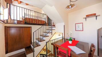 A staircase with a wooden finish, a dining area with a red tablecloth, and a wall-mounted shelf with a framed picture.