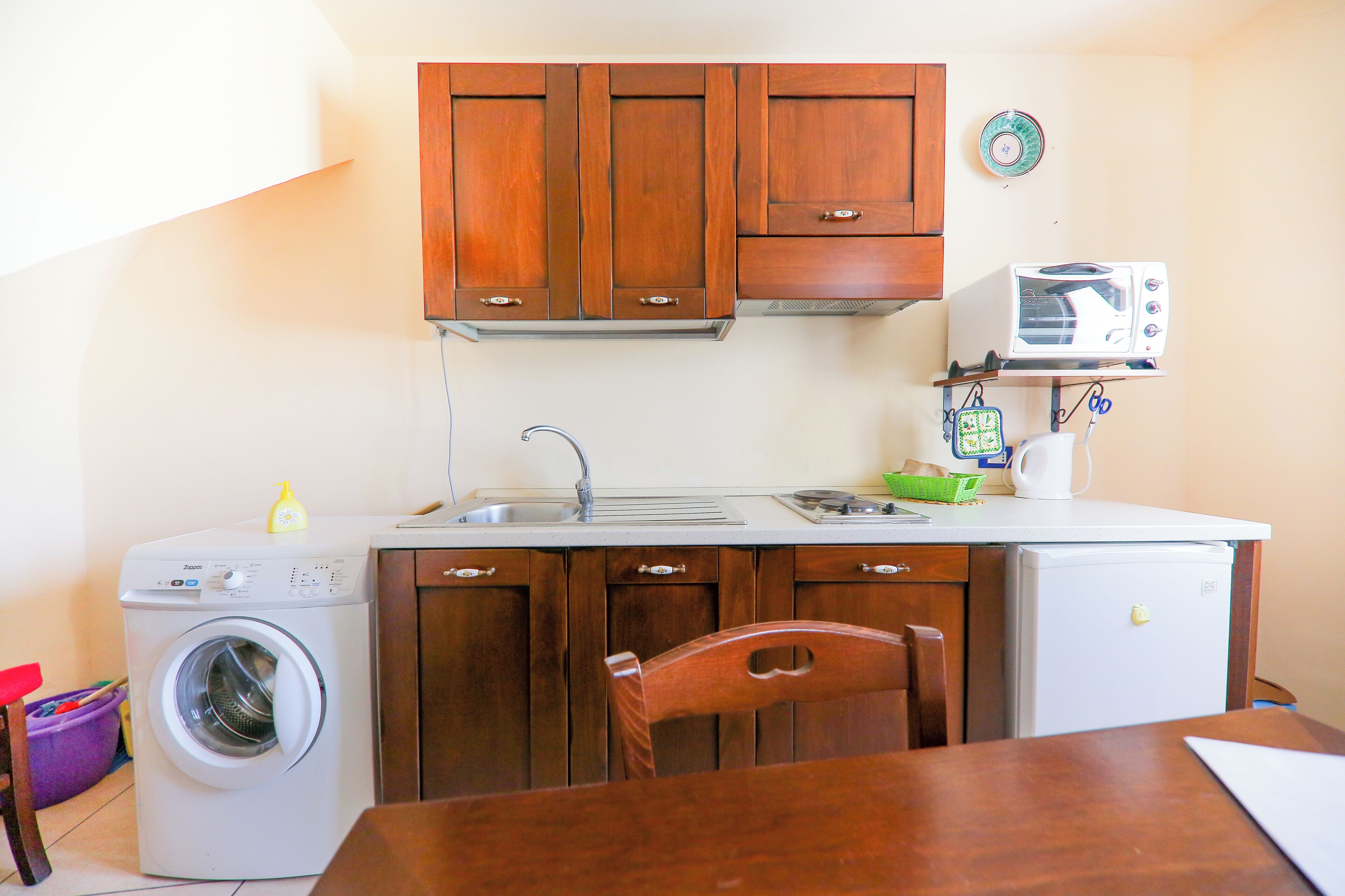 Cocina compacta con armarios de madera, lavadora, microondas y lavabo.