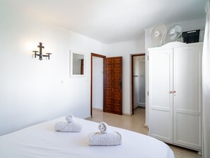 A bedroom with a bed, two towels, a wardrobe, a mirror, and a door leading to a bathroom. - Los Naranjos 15B Capistrano Village by Casasol by Interhome (Nerja)