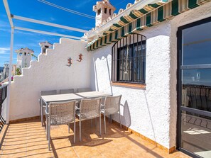 Eine Terrasse mit Tisch und Stühlen, ein Fenster mit Gitterstäben und eine weiße Wand mit Verzierungen.