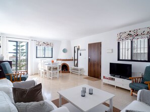 A living room with a fireplace, a television, and a dining area with chairs and a table. - Los Naranjos 15B Capistrano Village by Casasol by Interhome (Nerja)