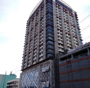 Ein Hochhaus mit mehreren Etagen, einer Werbetafel im Erdgeschoss und einer Baustelle zur rechten Seite.