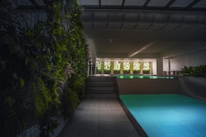 Ein moderner, überdachter Pool mit Fliesenboden und einer Wand üppiger Grünpflanzen.