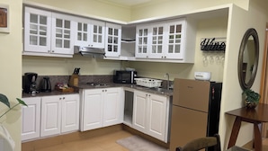 Una cocina compacta con armarios blancos, microondas, cafetera y refrigerador.
