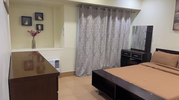 Un dormitorio con cama, cómoda, televisor y ventana con cortinas.