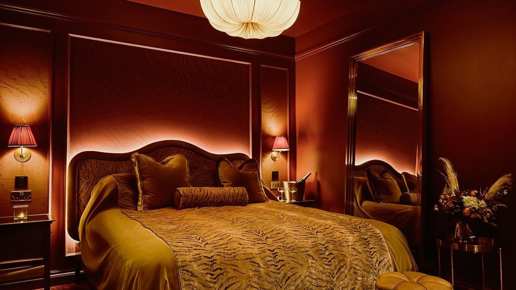 A luxurious bedroom with a large bed, a mirror, and a nightstand with a lamp.