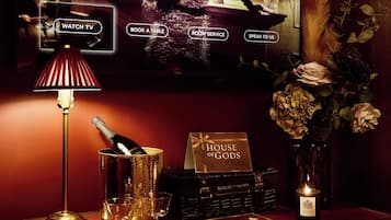 Un comptoir d’accueil d’hôtel avec un téléviseur affichant un menu, une lampe, une bouteille de champagne et un vase rempli de fleurs.