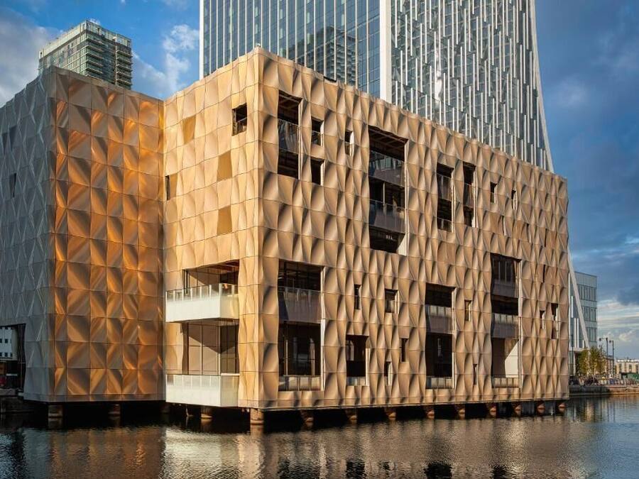 A modern building with a geometric facade, situated by a body of water.