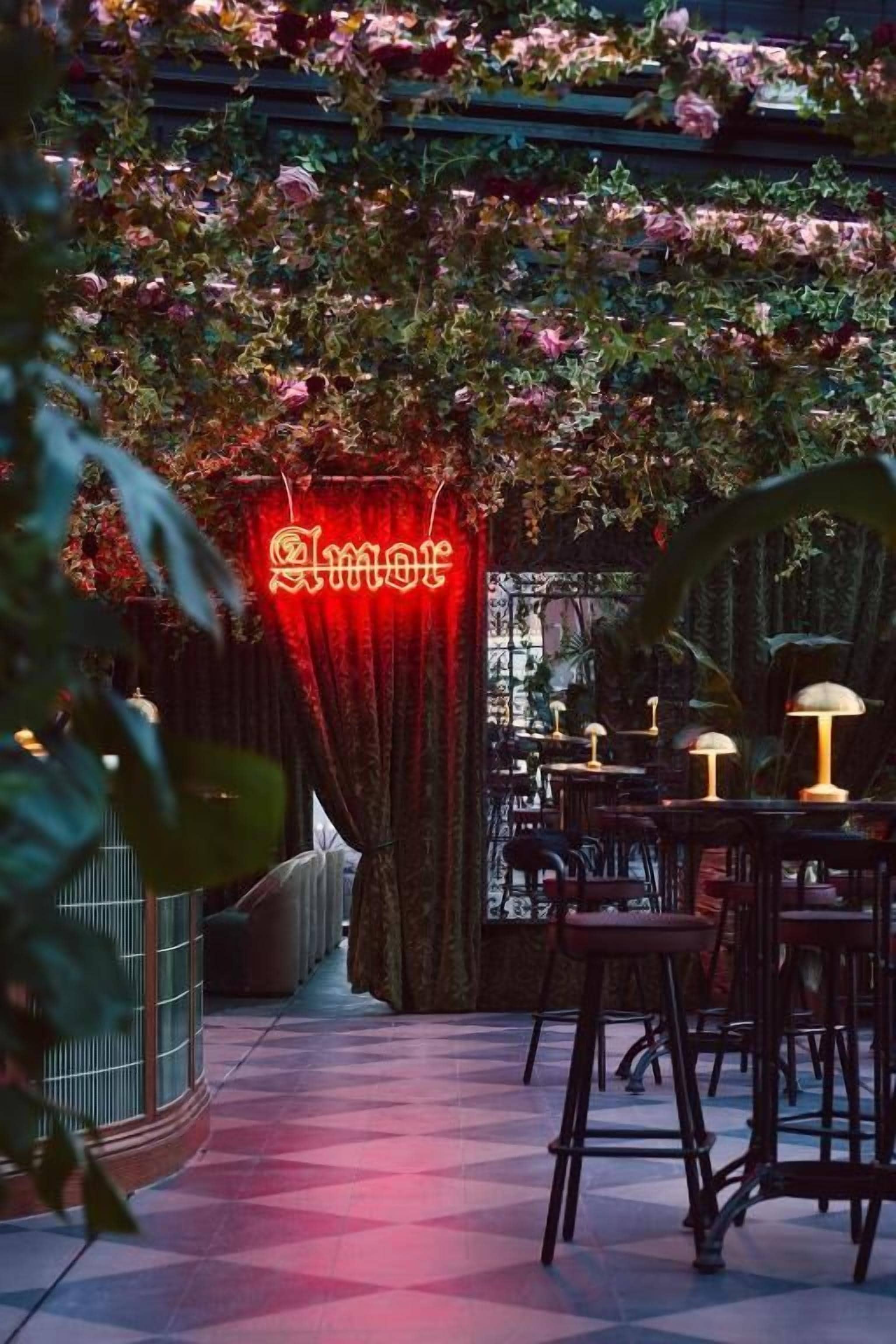 An indoor setting with a red neon sign, tables, chairs, and a patterned floor.