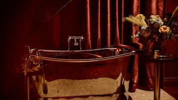 A bathtub with a glass enclosure, a small glass container, and a vase with flowers on a side table.