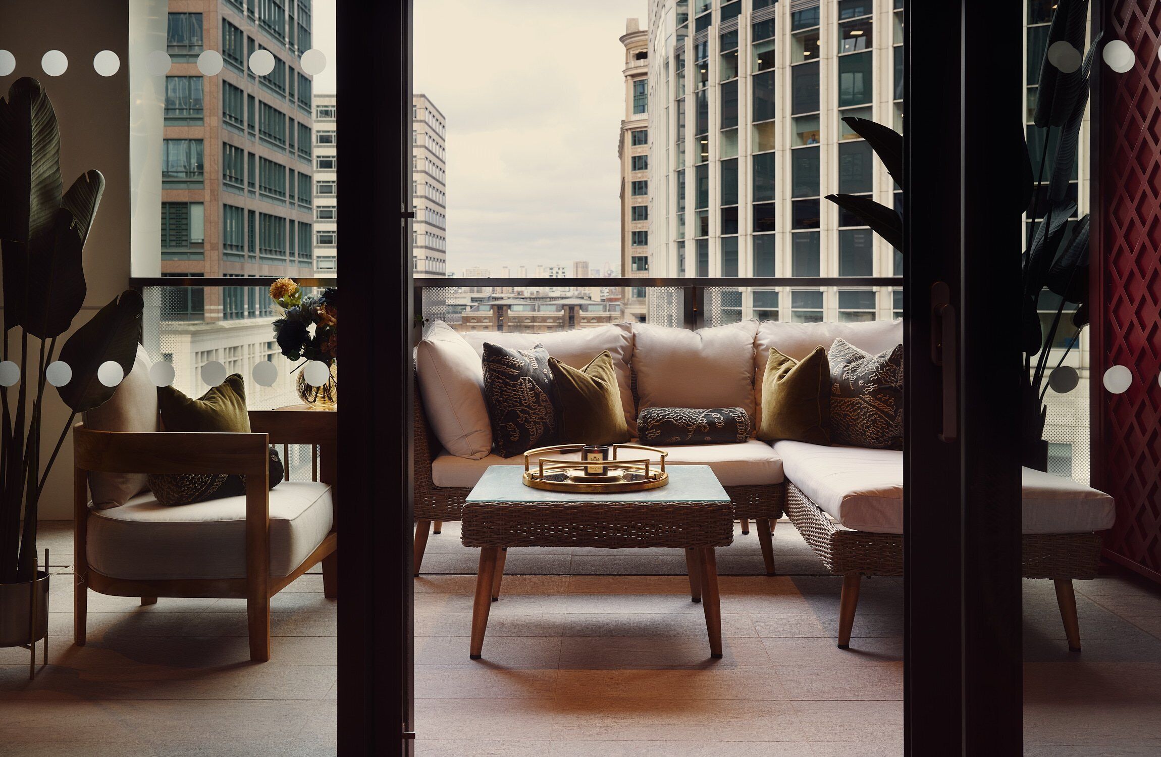 A balcony with a sofa, chairs, and a table, overlooking a cityscape.